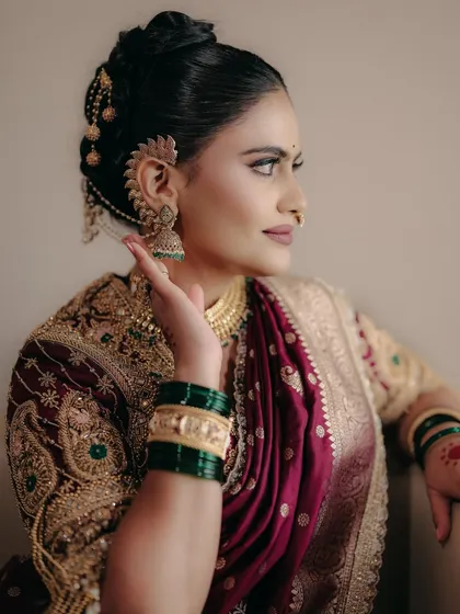 This profile view highlights the stunning traditional ear cuff and jhumkas. The makeup is kept clean and sharp to balance the ornate jewelry and heavily embroidered blouse.