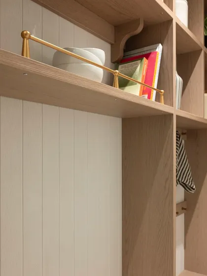 The brass railing on this open shelf is a small but elegant detail. It keeps cookbooks and decor items secure while adding a touch of warmth and sophistication to the wooden shelving.