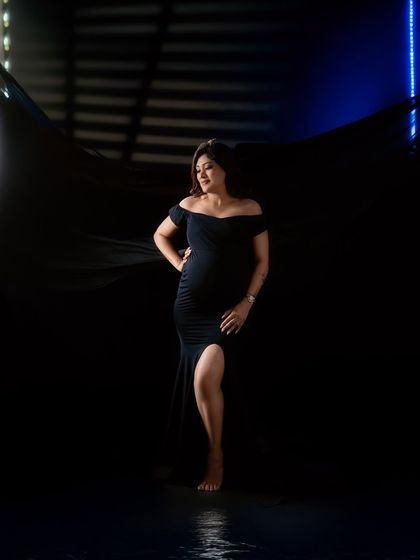 A full-length shot showcasing a sleek black maternity gown. The use of backlighting and a flowing black fabric creates a modern and high-fashion look.