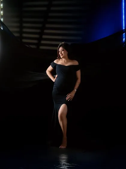 A full-length shot showcasing a sleek black maternity gown. The use of backlighting and a flowing black fabric creates a modern and high-fashion look.