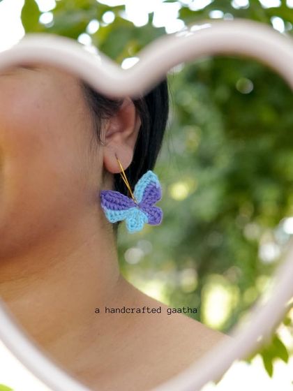 A model's reflection in a heart-shaped mirror, wearing the blue and purple butterfly earrings. It's all about those whimsical vibes.