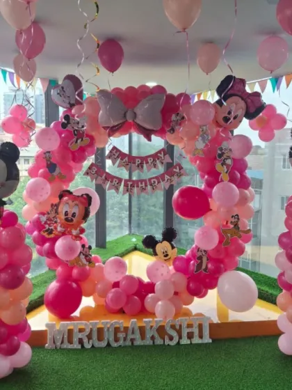 A full view of the Mickey and Minnie Mouse party on a green turf floor. The heart-shaped balloon arch and character balloon columns create a fun and inviting atmosphere.
