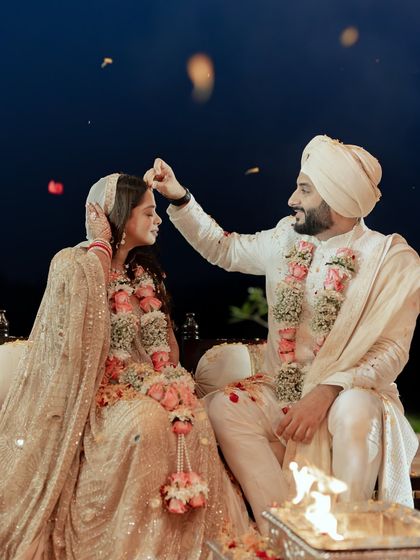 A tender moment during a Sikh wedding ceremony. The groom places his hand on the bride's head in a gesture of blessing and love, captured beautifully under the night sky.