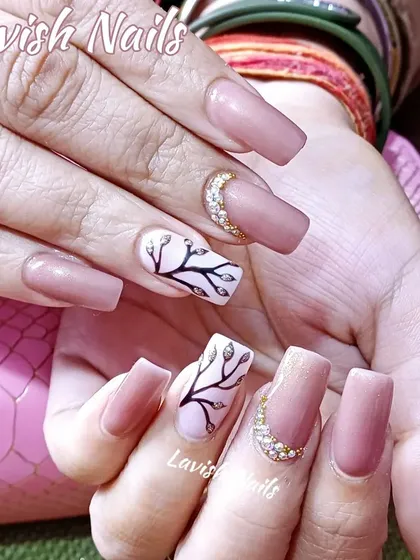 Muted pink nails with gold rhinestone crescent moons and hand-painted tree branch art.