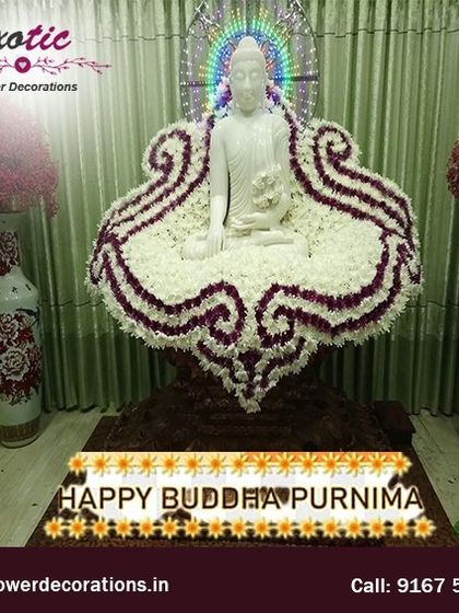 A serene and respectful floral arrangement for Buddha Purnima. A white Buddha statue is placed on a throne of white flowers with purple accents, creating a peaceful and meditative focal point.