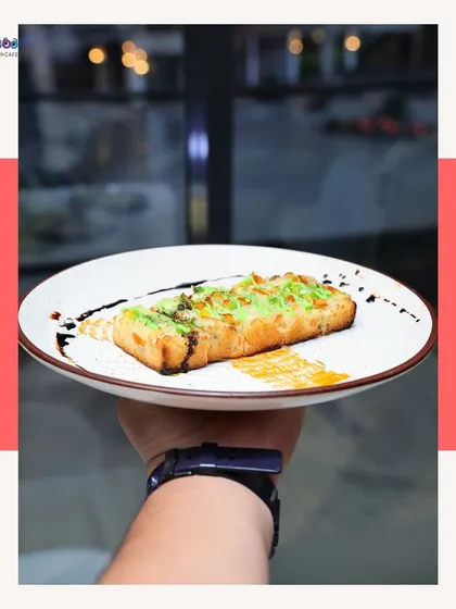 A hand holds up a plate of our cheesy garlic bread. It's a classic comfort food, elevated with high-quality cheese and a perfect garlic flavor, then drizzled with balsamic for a gourmet touch.