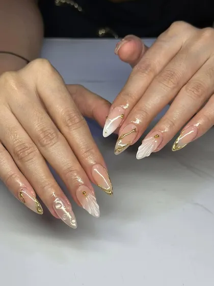 An elegant design with a mix of textures. These stiletto nails feature a nude base with gold chrome tips and delicate, sculpted 3D shell accents.