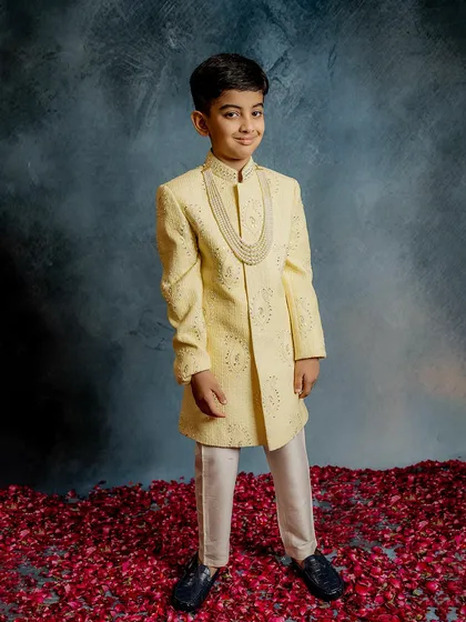 Dressed in our pale yellow sherwani, this young model looks ready for any grand celebration. The outfit is accessorized with a pearl necklace, enhancing its regal and festive feel.