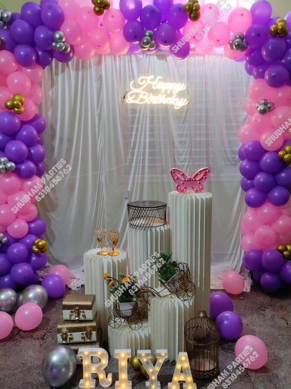 A beautiful birthday stage with a pink and purple balloon arch, white curtain, and elegant props.
