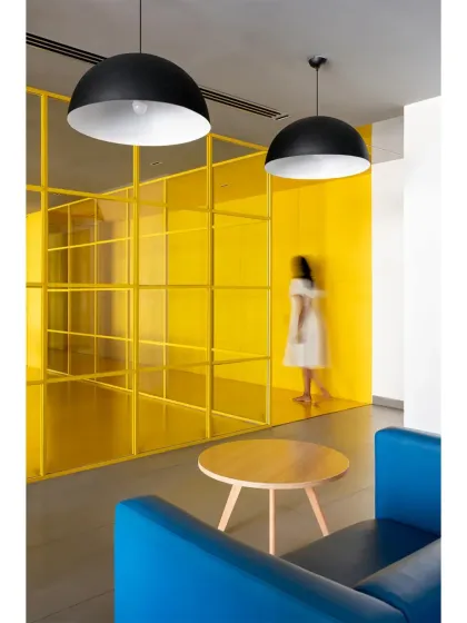 The lounge area in 'The Amber Encase' uses a yellow-tinted glass partition to separate spaces while maintaining visual connection. The large dome pendant lights anchor the seating area.