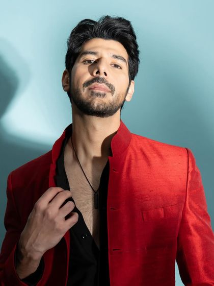 A close-up portrait of actor Pavail Gulati. The lighting is focused to highlight his sharp features against the cool blue studio background.
