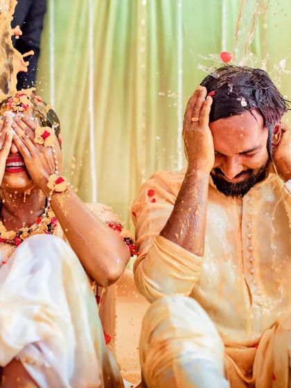 A playful moment during the Haldi rituals, with the couple covering their faces as they get splashed with turmeric water.