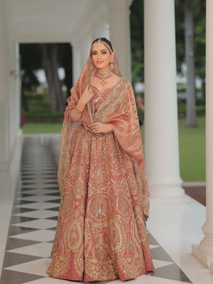 An elegant heritage look in a dusty rose lehenga with intricate gold threadwork. This is a beautiful alternative to traditional red, offering a softer yet equally regal feel.