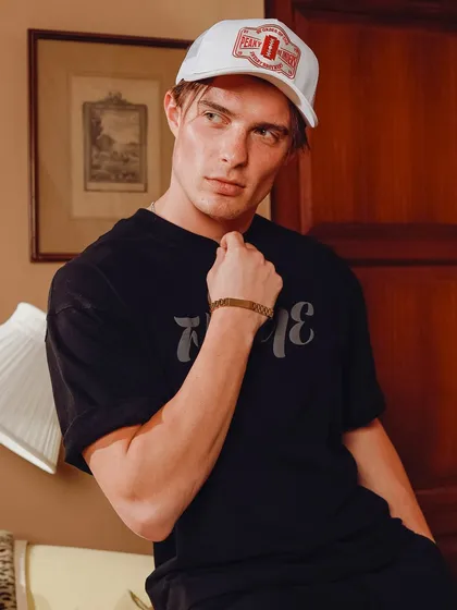 A portrait-style shot focusing on one model. The lighting highlights the texture of the cap and the model's expression, creating a cool, vintage vibe for this apparel brand's campaign.