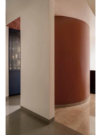 The bar enclave in Apartment 1005 is defined by a bold, curved wall in a deep terracotta hue. This architectural element creates an intimate and sophisticated niche, separating the bar from the main living space while maintaining a visual connection.