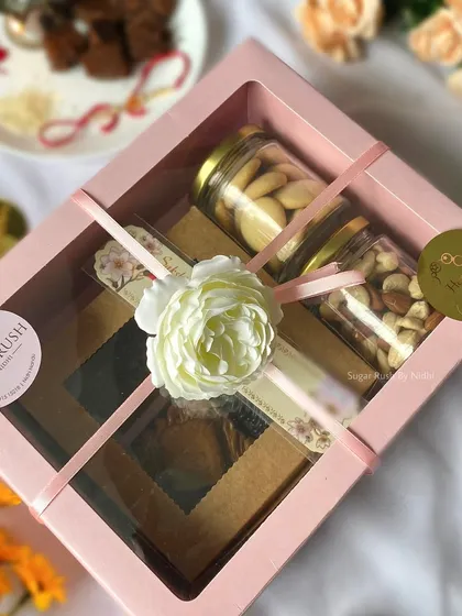 The 'Raksha Delight' hamper, beautifully packed with a floral touch. It includes assorted brownies, roasted nuts, and butter cookies.