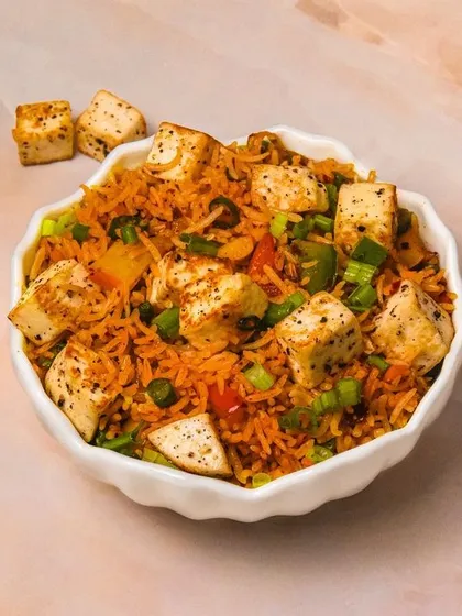 A bowl of savory paneer fried rice, shot on a light marble background. The clean presentation focuses on the chunks of paneer and vegetables in the dish.
