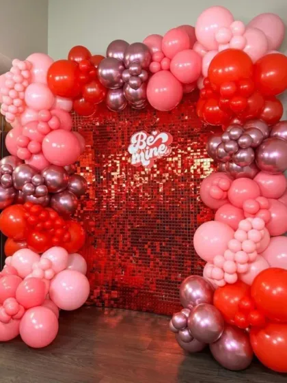 A glamorous 'Be Mine' backdrop for Valentine's Day. The red sequin wall framed by a pink and red balloon arch is perfect for a romantic surprise.