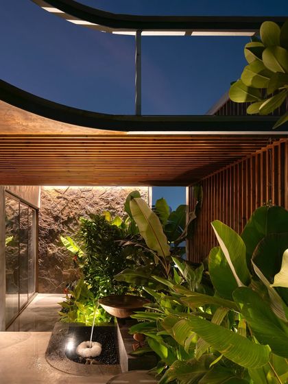 A rooftop terrace at night, where a water feature and surrounding plants are beautifully illuminated. The lighting design creates a tranquil and magical atmosphere, perfect for evening relaxation.