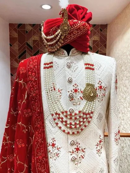 A classic groom's choice. This is an ivory white sherwani with intricate red floral embroidery, paired with a matching red pagri and a velvet stole. This complete set is available for rent and guarantees a majestic look.