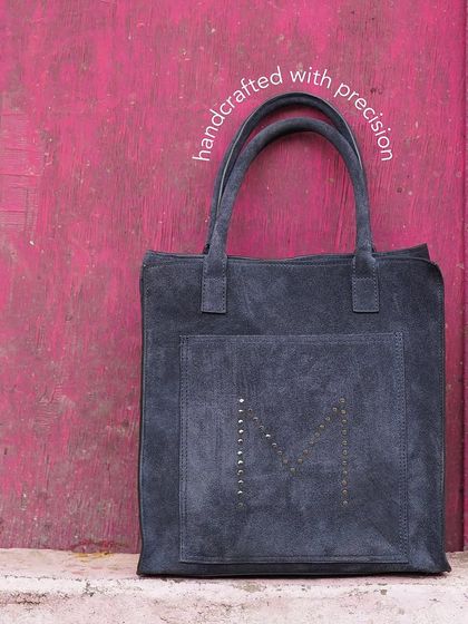 A spacious and sturdy suede tote, ideal for your travel needs. This version in grey suede features a hand-studded 'M' pattern for a subtle branding touch.