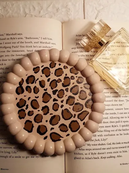 A hand-painted bubble tray with a classic brown leopard print design, styled on an open book.