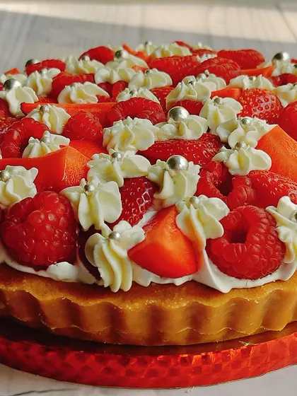 The side profile of the mixed berry cheesecake tart reveals its thick, buttery crust and the generous pile of fresh fruit and cream on top.