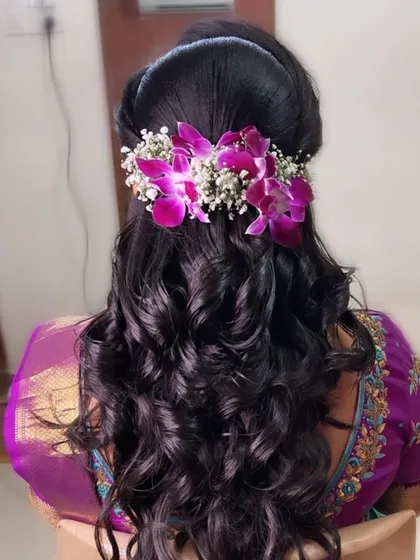 For a modern reception, soft curls and fresh flowers create a romantic and elegant hairstyle. This look features voluminous curls cascading down, accented with delicate purple orchids and baby's breath. It's a beautiful way to blend contemporary style with a touch of natural grace.