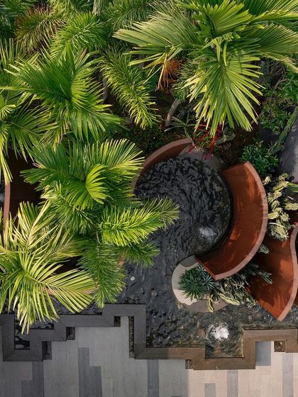 A top-down shot of the curving Corten steel walls at KEUS, surrounded by palm trees. This perspective reveals the intricate, snake-like layout of the installation and its relationship with the surrounding greenery.