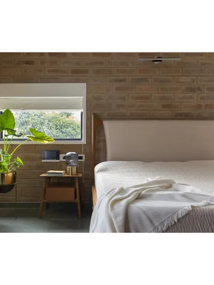 A bedroom in the renovated Hyderabad residence. The exposed brick wall adds warmth and texture, while the simple window frames a view of the surrounding greenery, creating a calm and restful atmosphere.