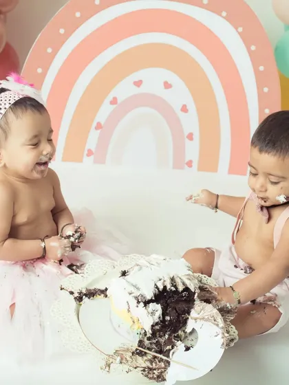 Double the fun, double the mess! These adorable twins share a laugh and a cake during their colorful rainbow-themed first birthday cake smash.