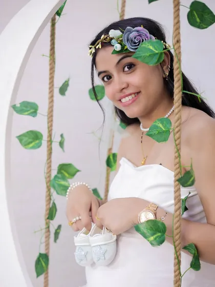 A close-up shot focusing on the details. The mom-to-be holds a pair of tiny baby shoes, her smile and the floral headband adding to the joyful feel of the announcement.