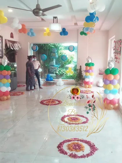 The indoor setup for the welcome baby boy party. The room is filled with rainbow-colored balloon pillars and flower rangoli on the floor, creating a bright and cheerful atmosphere.
