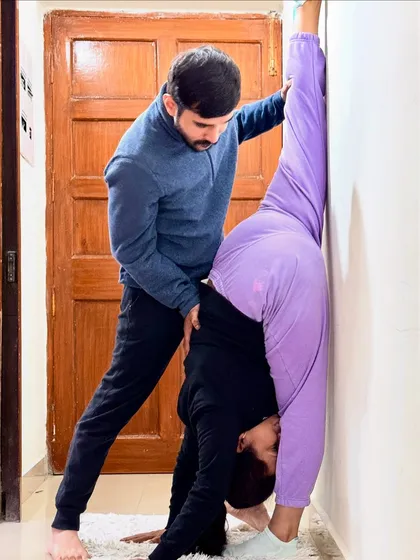Using the wall as a prop for Urdhva Prasarita Eka Padasana (Standing Split Pose). I am helping my student deepen the stretch in her hamstrings while keeping her hips square and aligned.