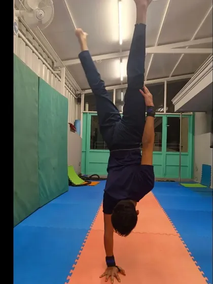 A student holding a one-handed handstand. This is an advanced skill that requires an incredible amount of shoulder stability, wrist strength, and balance.
