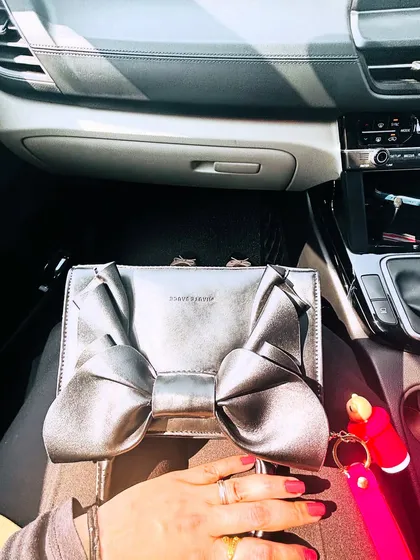 A shot focusing on a unique silver bow-shaped clutch, taken in the car. This highlights a statement accessory.