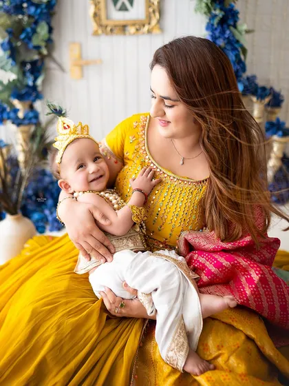 This mamma is glowing with happiness as she holds her little Krishna, dressed in a bright yellow outfit.