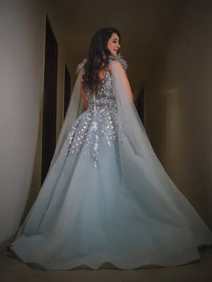A fairytale moment. This shot from behind shows the bride's magnificent reception gown with its flowing cape, creating a sense of drama and elegance as she walks down the corridor.