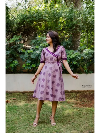 A dynamic full-length shot of the actress in a garden. Her pose is playful and full of life, showcasing the movement and style of her wrap dress.