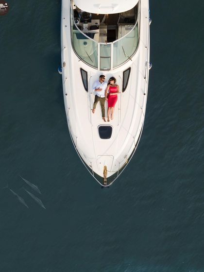 A perfectly composed drone shot of a couple lying on the bow of a yacht. The clear blue water and the symmetry of the boat make this a clean, modern, and luxurious pre-wedding photo.