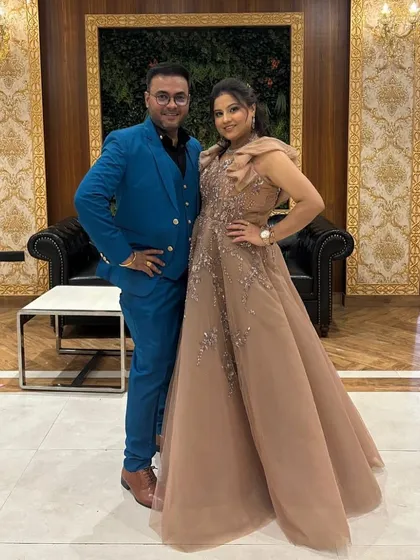 A happy couple ready for a celebration. She is wearing an elegant beige gown with delicate shoulder details, a perfect example of the sophisticated party wear available in our pre-owned collection.