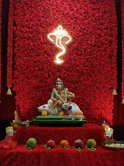 This modern Ganpati setup features a textured red backdrop with a neon Ganpati silhouette. The hanging bells and simple red cloth on the platform complete this stylish and contemporary look.