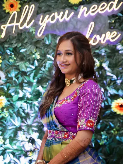 A vibrant and colorful Haldi look. The bride's makeup is fresh and glowing, with a focus on enhancing her beautiful smile against a fun, floral backdrop.