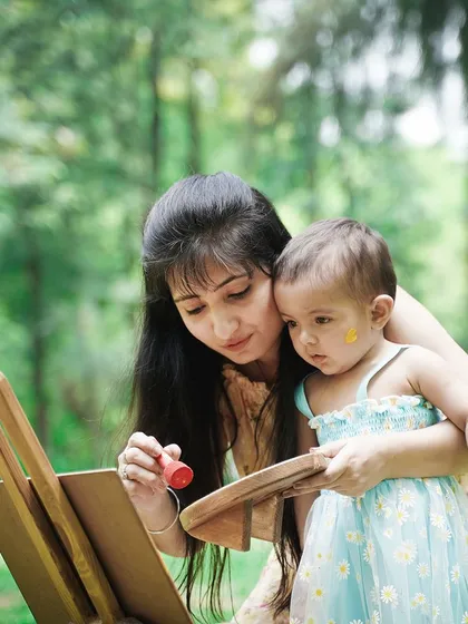 A mother and her baby daughter have fun with an easel and paints during a creative outdoor session.