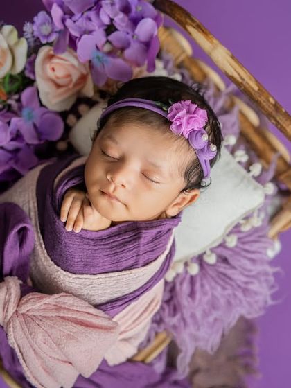 An overhead view of the baby resting in a miniature swing, surrounded by a cascade of purple and pink flowers. This setup creates a whimsical and enchanting portrait.