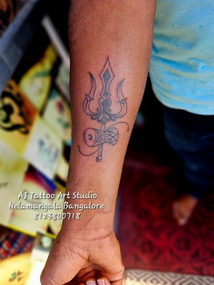 A finely detailed tattoo of a Trishul with a Damaru on the forearm.