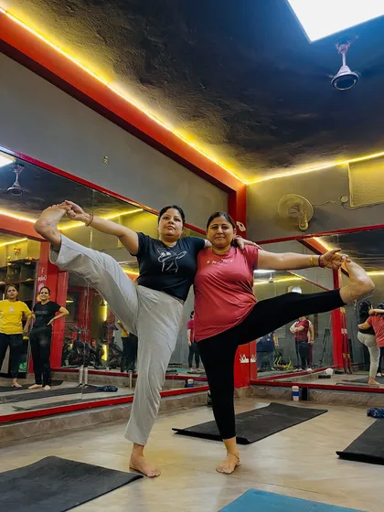 Two participants enjoying a partner standing split pose. My classes are a space for fun, encouragement, and shared achievement.