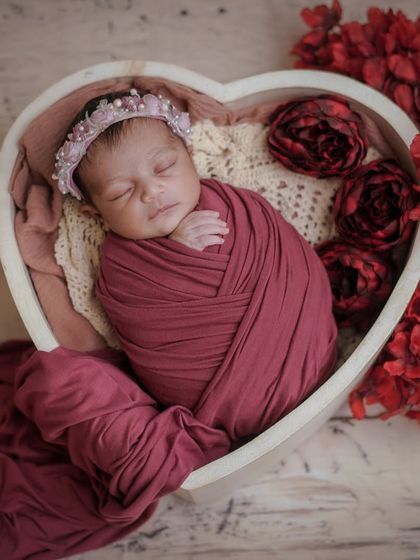 A heart of roses. This beautiful setup places a swaddled baby in a heart-shaped bowl, surrounded by rich red fabric and flowers.