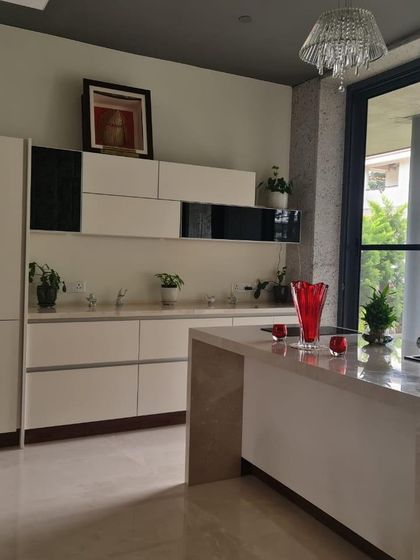 A real-life view of a completed kitchen project, featuring a white island and cabinetry with black accents. The large glass door opens to the outside, flooding the space with natural light.
