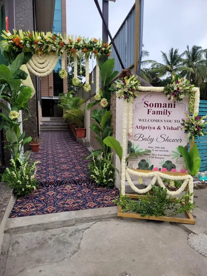A beautiful entrance arrangement for a baby shower, featuring a floral arch with hanging jasmine strings and a personalized welcome sign for the family. The pathway is lined with greenery to guide guests into the venue.